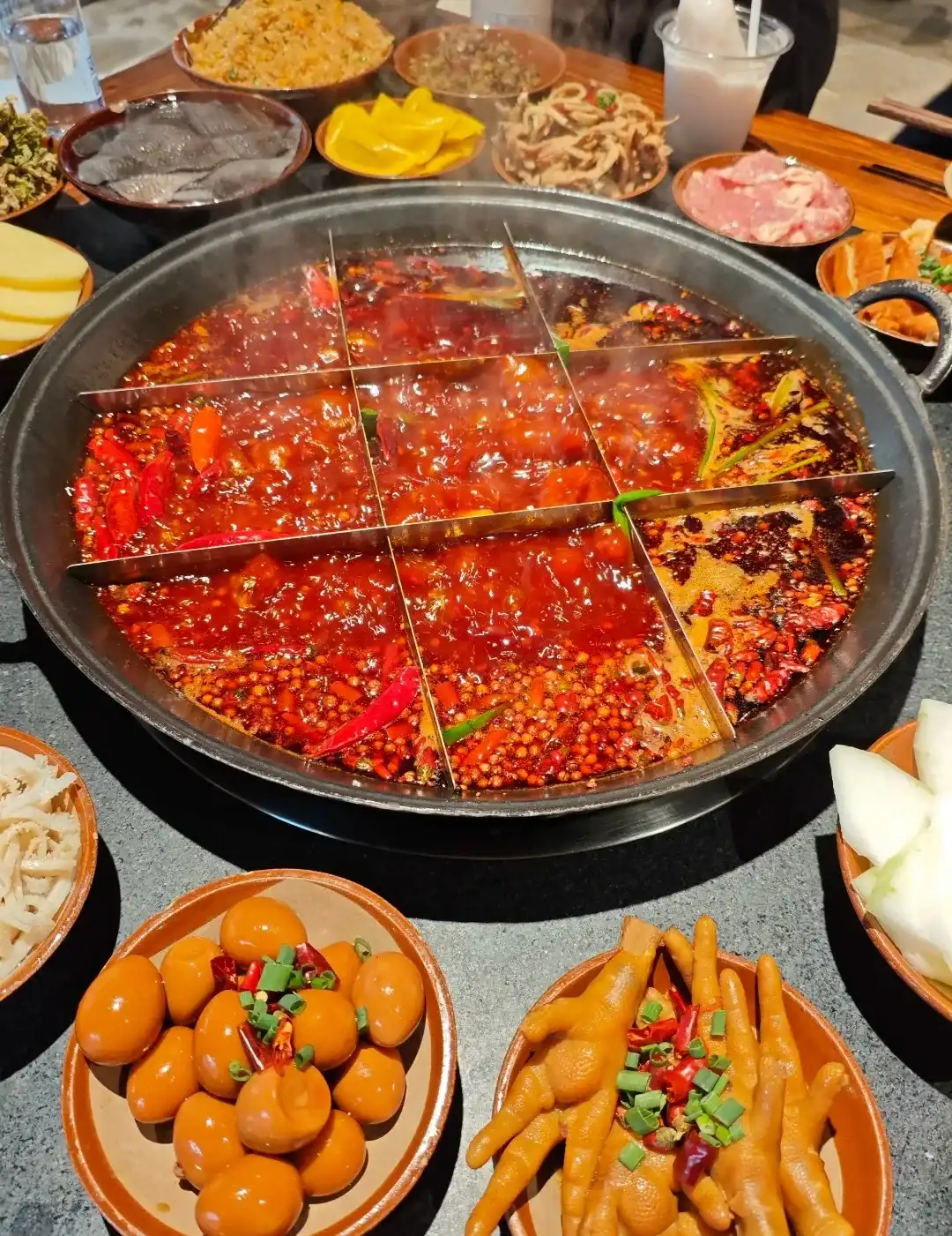 A boiling nine-grid Chongqing red-broth hot pot surrounded by dishes