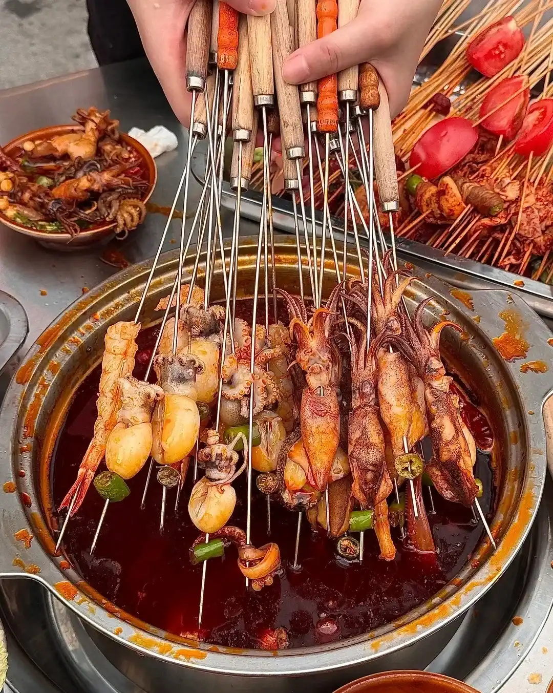 Small skewers of meat and vegetables arranged beside a red Chengdu chuanchuan pot