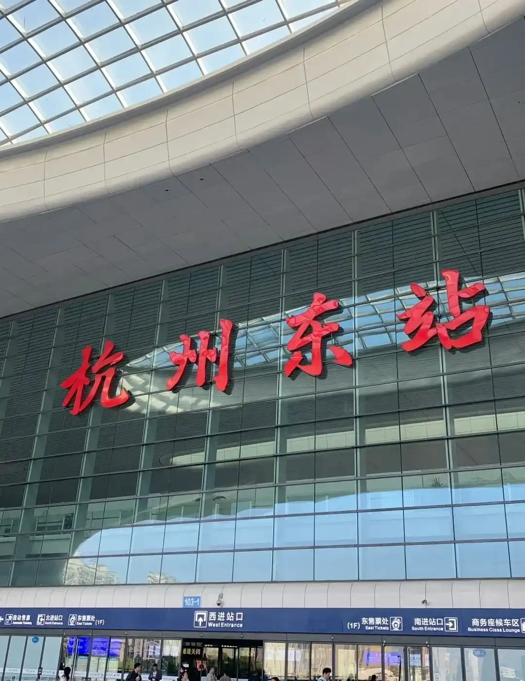 Travelers beneath the red station sign at the west entrance of Hangzhou East Railway Station