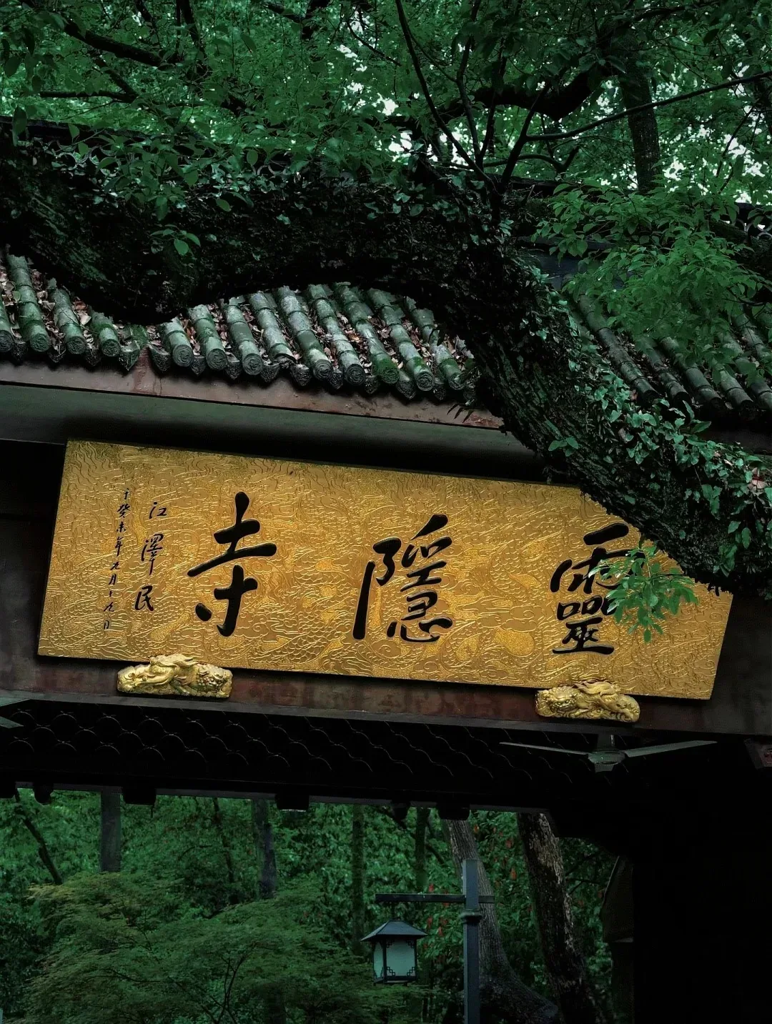A gold Lingyin Temple sign beneath the trees
