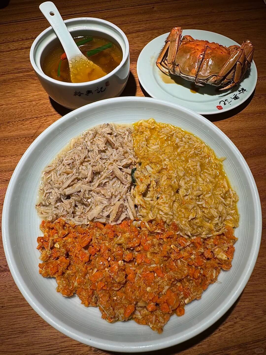 Crab meat, roe and paste arranged beside noodles, with a cooked crab and soup behind